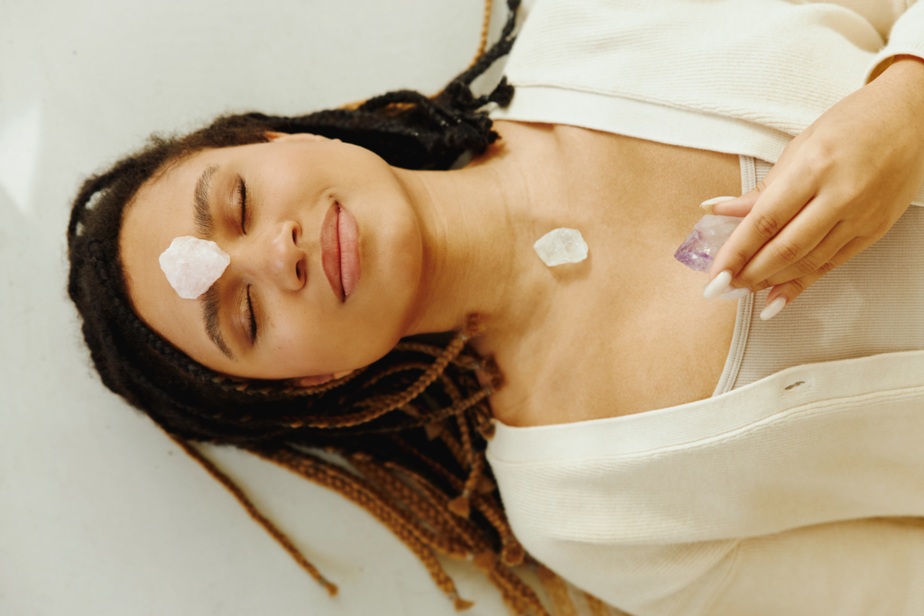 Attractive young woman meditating with eyes closed and gemstones on top of forehead and chest. Top view.
