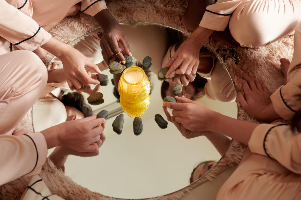 Hands of young women putting pebbles around burning candle on round mirror when fortune telling