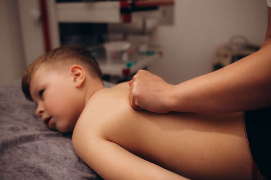 A little boy relaxes from a therapeutic massage. Male massage therapist makes a medical massage to the back of a child