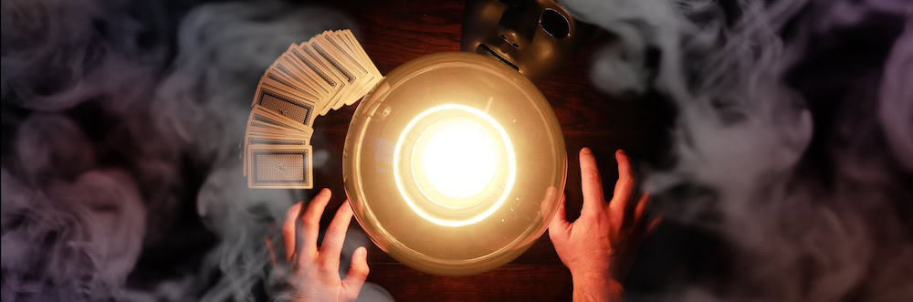 Overhead shot of a glowing crystal ball and hands surrounded by smoke and cards.