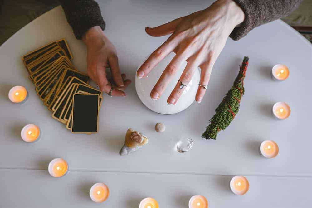 Overhead view of a mystical table setup with a glowing crystal ball, tarot cards, and sage.