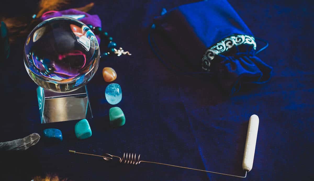 A crystal ball, polished gemstones, and a ritual dowsing rod arranged on a dark blue velvet cloth.